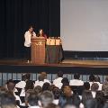 Two speakers stand at podium in front of a large crowd