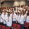Crowd in white coats stands and reads from cards