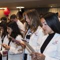 Crowd in white coats stands and reads from cards