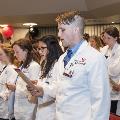 Crowd in white coats stands and reads from cards