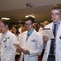 Crowd in white coats stands and reads from cards