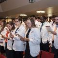 Crowd in white coats stands and reads from cards